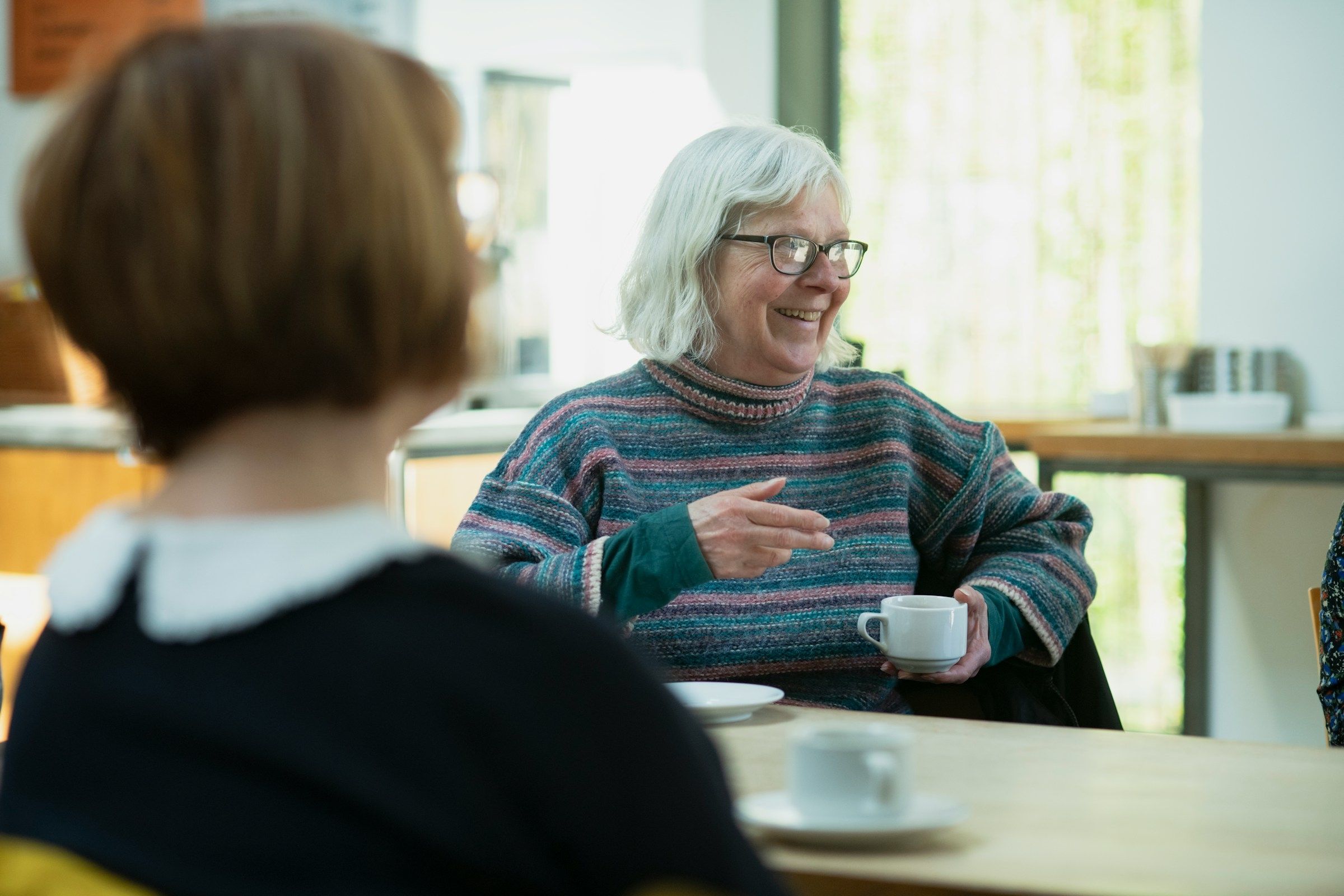 Caregiver and an older woman laughing together over cups of coffee