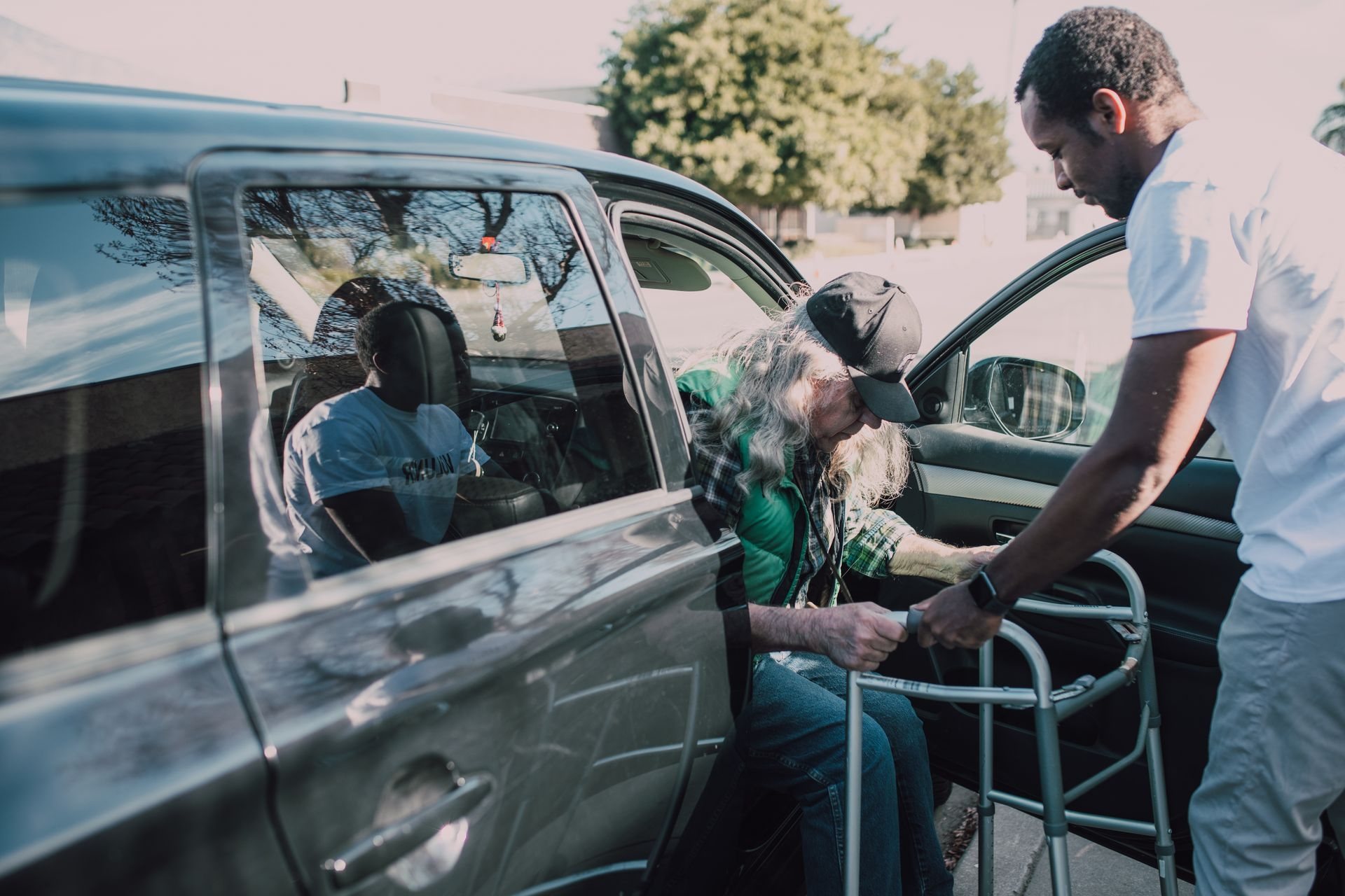 Caregiver steadying a walker as an older man gets out of a car